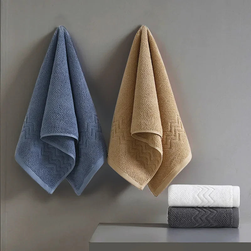 Set of blue, beige, white, and gray textured towels on a gray wall.