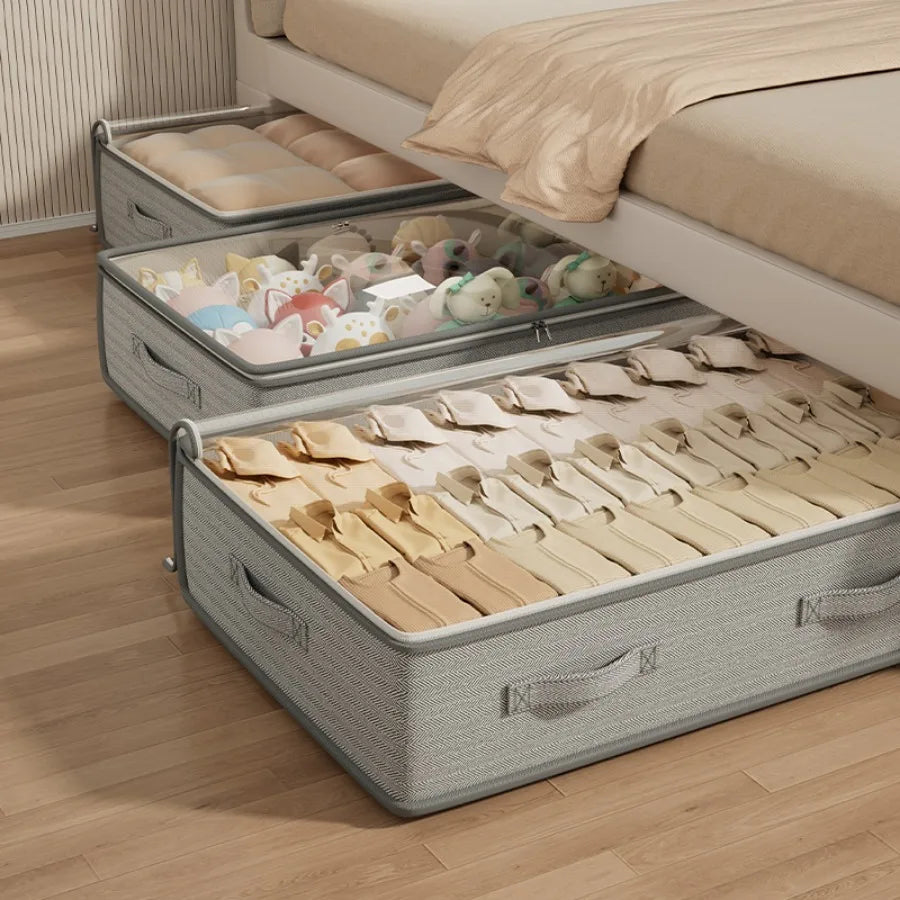 Gray storage bins under a bed with toys and clothes inside, on a wooden floor.