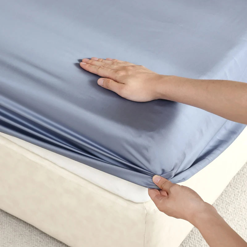 Person stretching a light blue fitted sheet over a bed