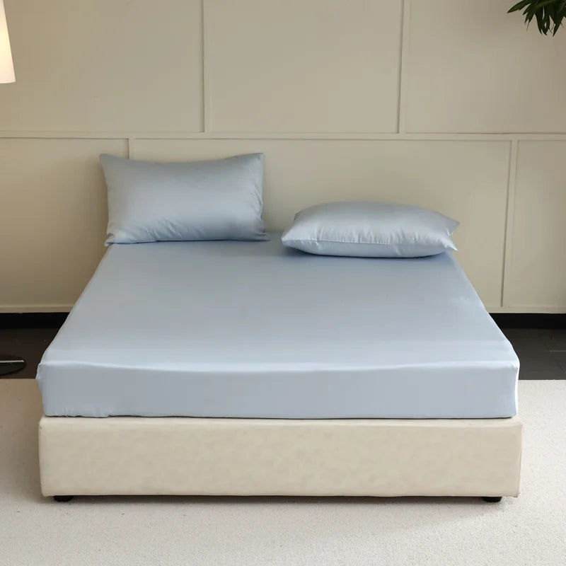 Bed with light blue mattress cover and pillows against a beige wall.