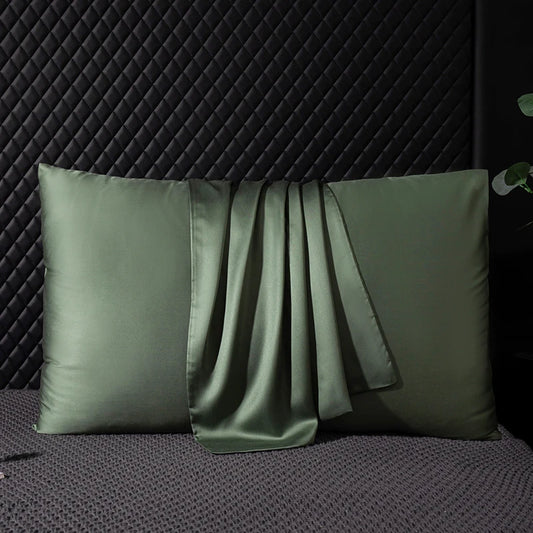 Two green satin pillows on a textured surface with a dark background