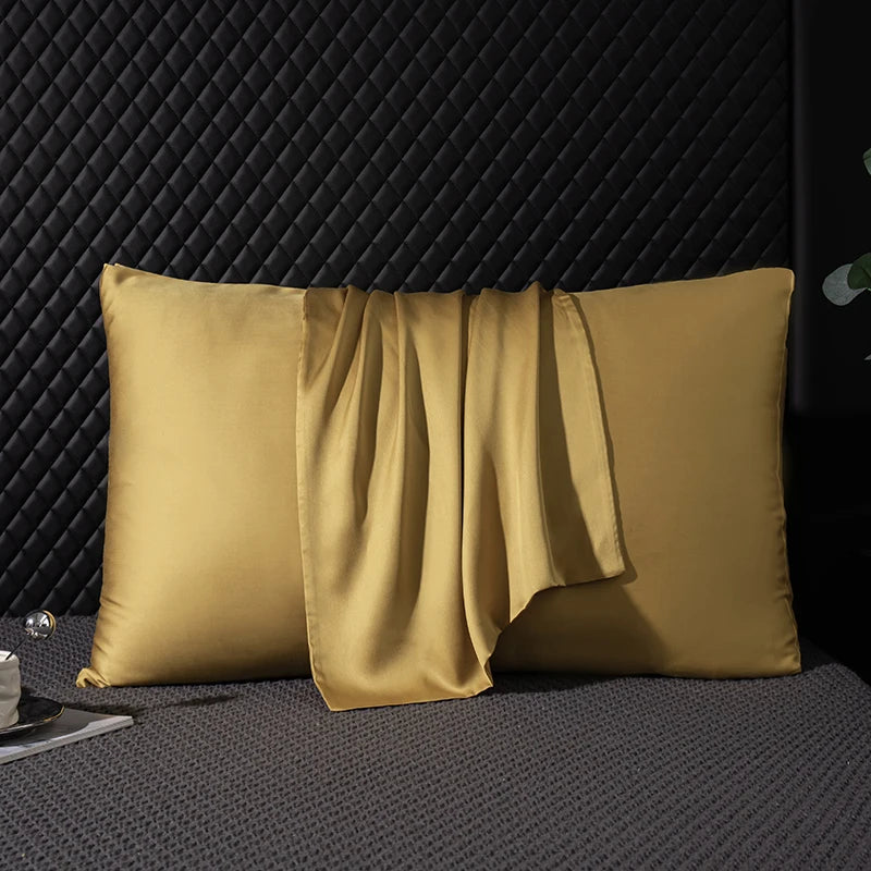 Two gold satin pillows on a textured dark surface with a black textured wall background.