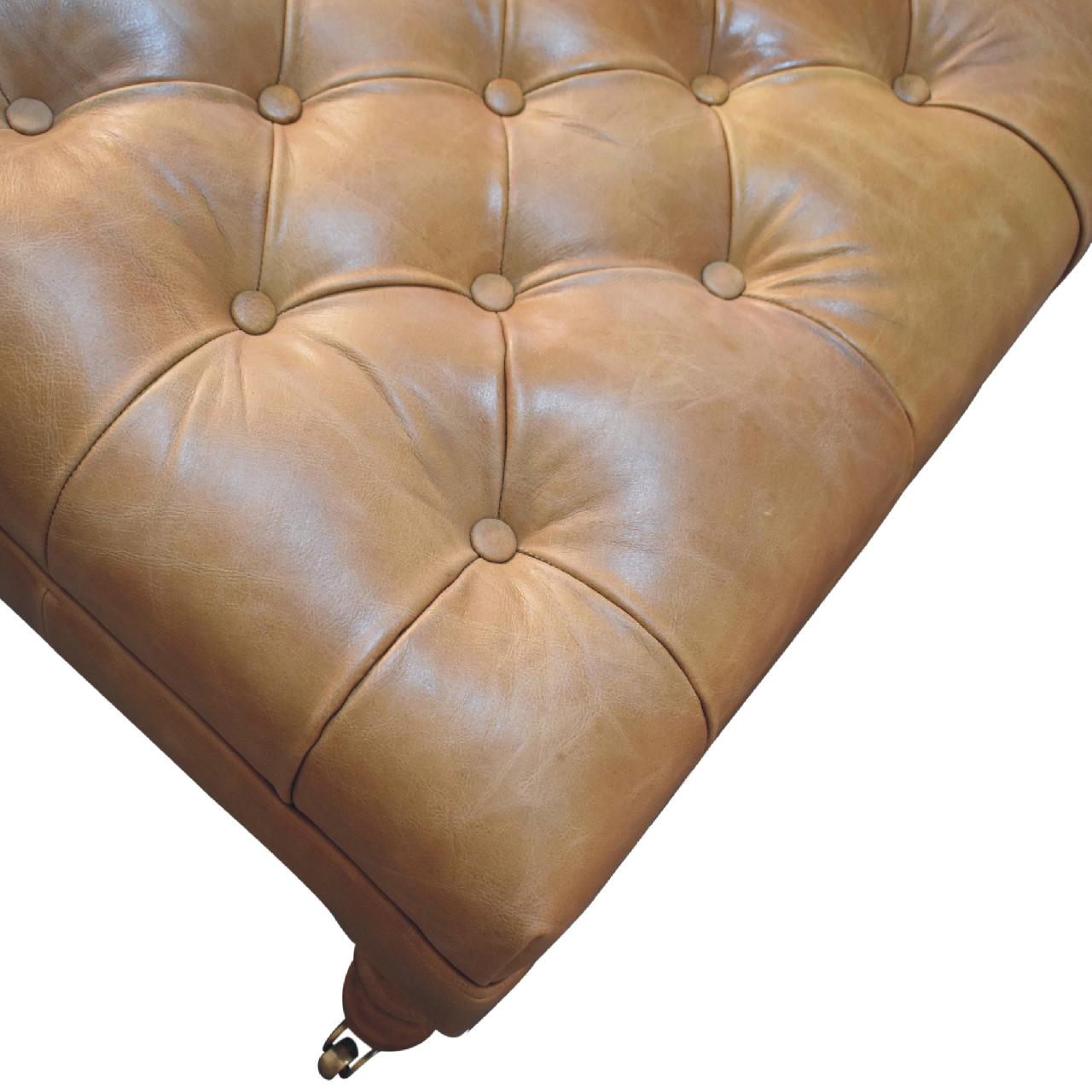 Tan buffalo leather ottoman with solid mango wood base, deep-buttoned top, and light walnut hand-turned feet. Deep button view.