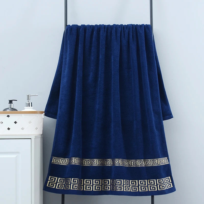 Blue towel with decorative border hanging on a rack against a white wall.