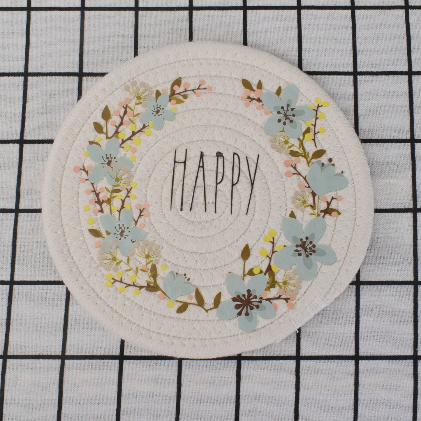 Round woven coaster with floral design and 'Happy' text on a grid background
