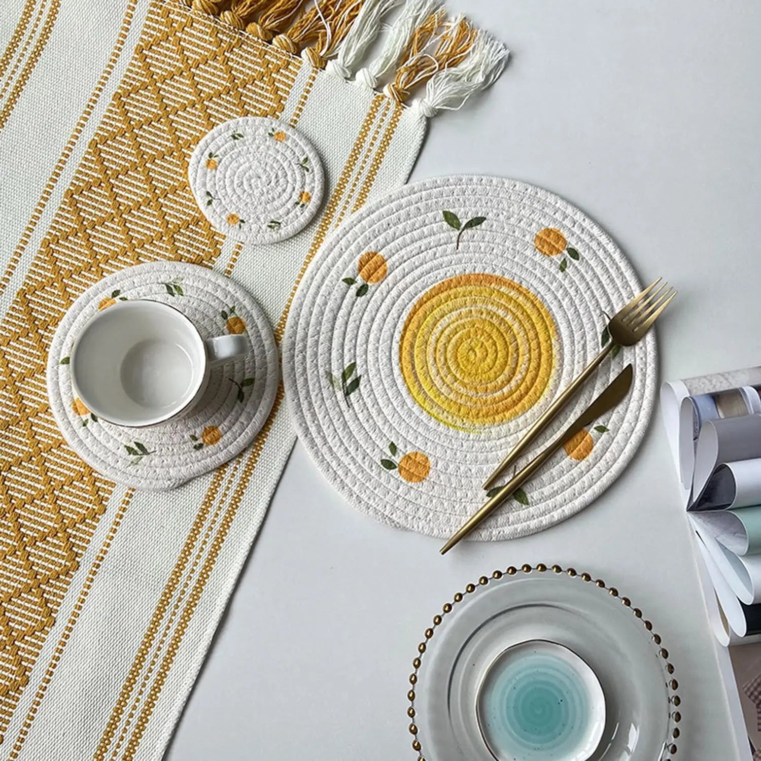 Decorative table setting with woven placemats, cutlery, and tea set on a white surface.