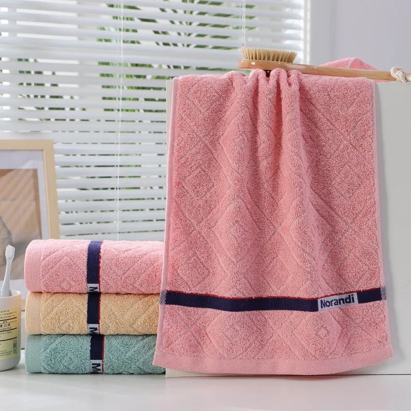 Set of pink, beige, and green towels with a broom on a white surface.