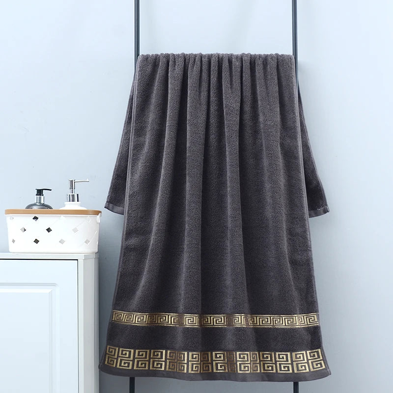 Dark gray towel with decorative border hanging on a rack in a bathroom setting.