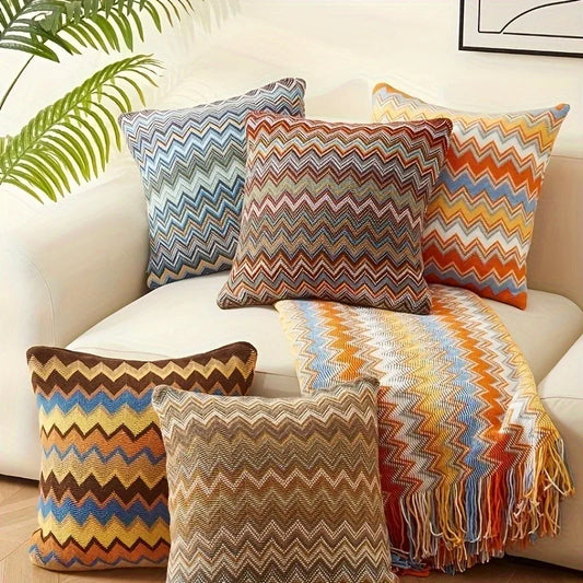 Colorful zigzag patterned pillows and a blanket on a sofa with a plant in the background.