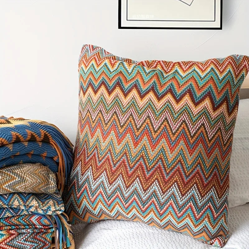 Colorful zigzag patterned pillow on a sofa with a blanket and framed picture in the background.