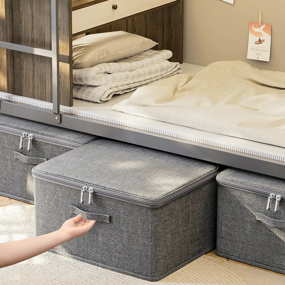 Gray storage boxes with handles on the floor next to a bed with folded bedding.