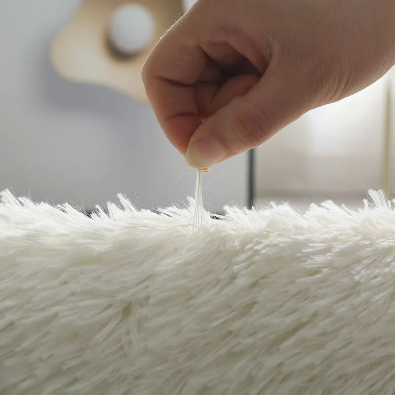Close-up of a hand stretching a strand of white yarn over a fluffy white surface.