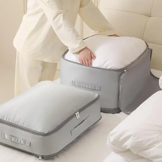 Person using a gray travel pillow on a bed with another gray suitcase nearby.