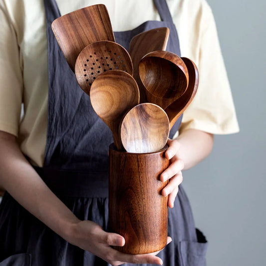 Person holding a wooden utensil holder with various wooden spoons and ladles.