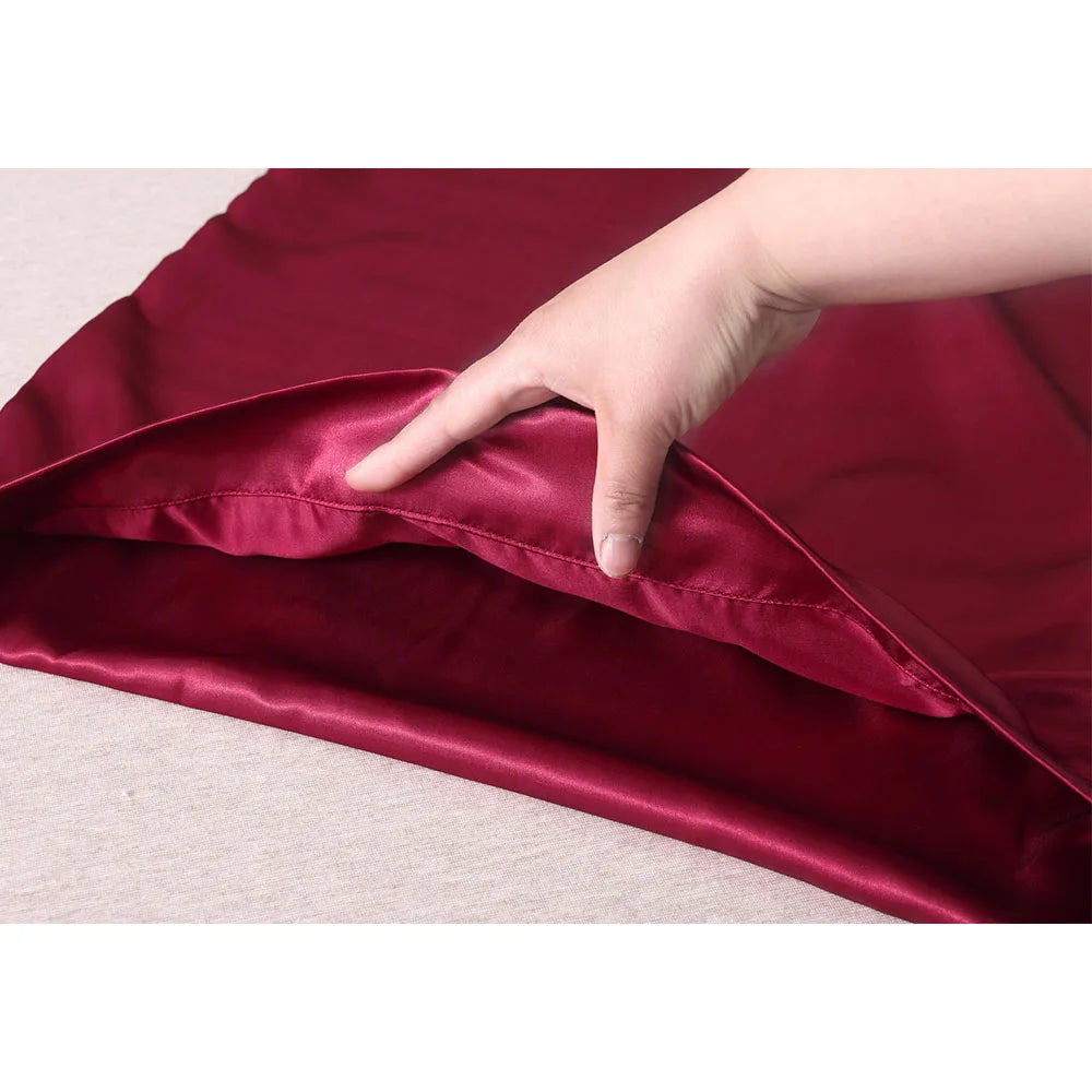 Hand touching a burgundy satin pillowcase on a light background