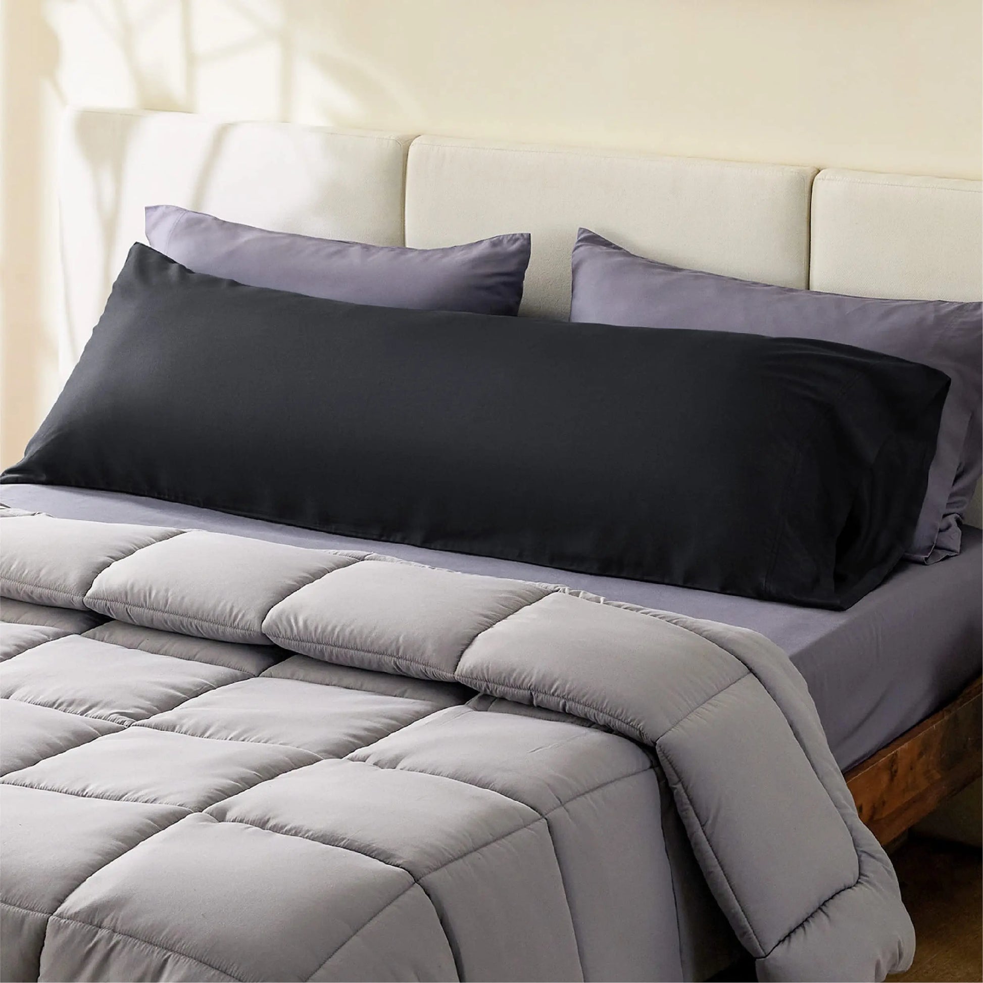 Black satin pillowcase on a bed with gray comforter and pillows.