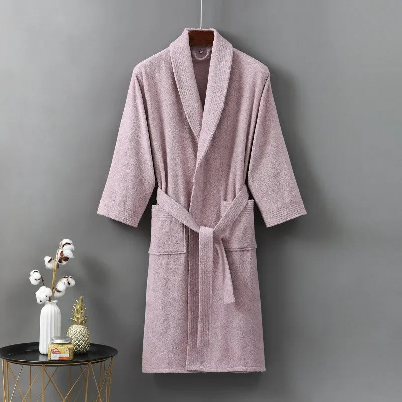 Pink bathrobe hanging on a gray wall with decorative items on a small table.