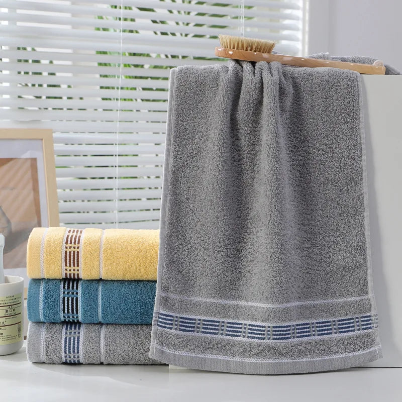 Gray towel with blue stripes on a white surface, with other towels and a brush in the background.