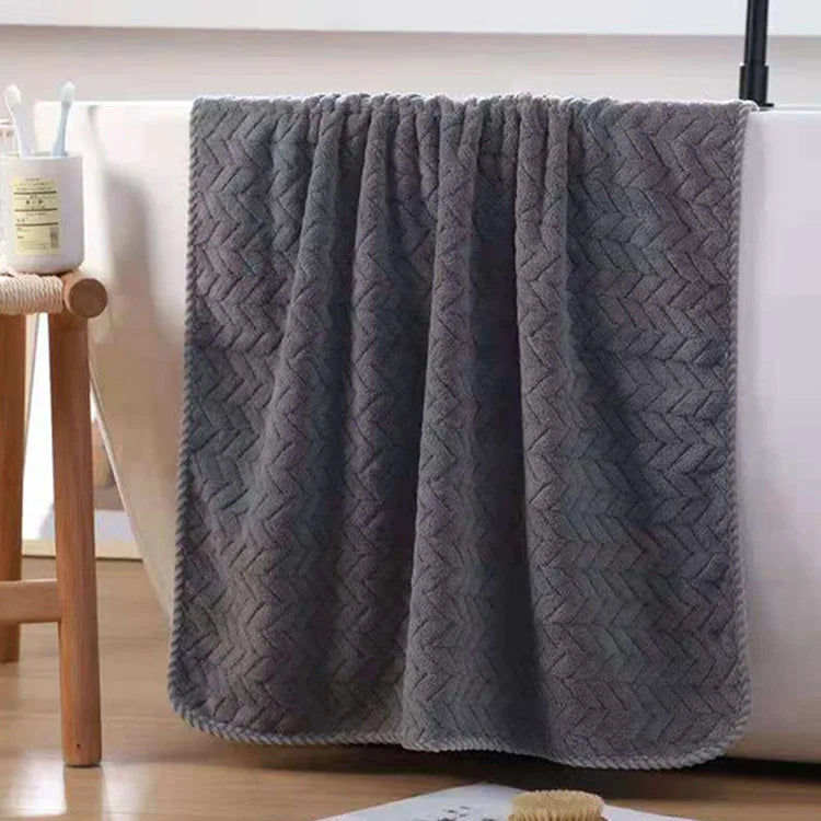 Gray textured blanket draped over a white surface with a wooden stool and candle in the background.