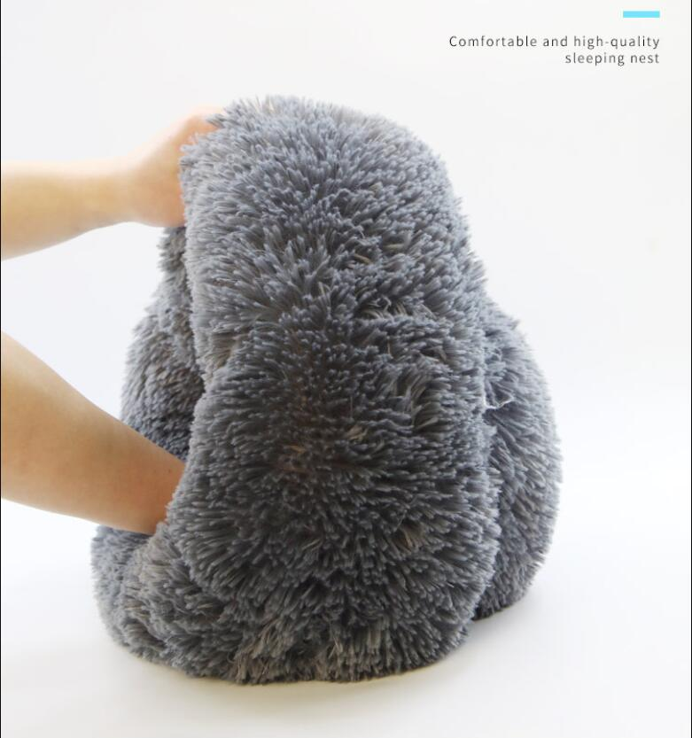 Gray plush pillow being held by a hand on a white background