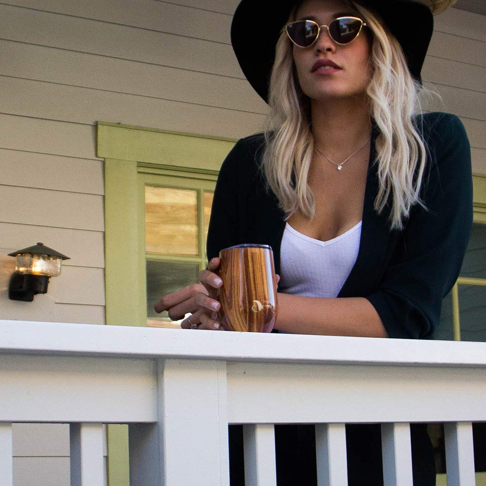 Woman holding a glass on a porch with a house in the background