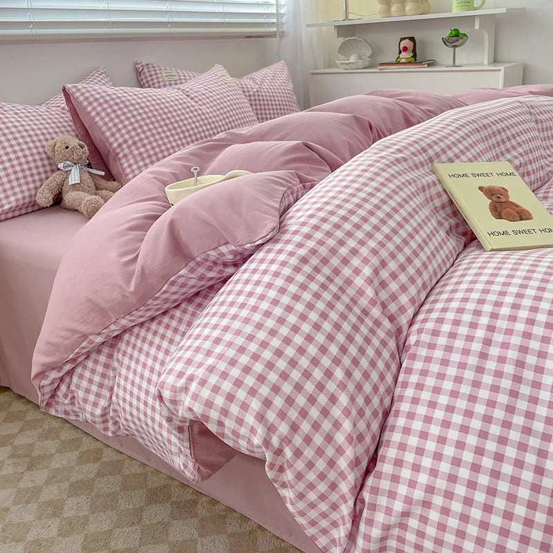 Pink checkered bedding set on a bed with a teddy bear and book in a bedroom.