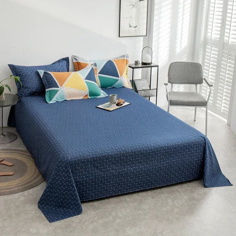 Bed with blue bedding and colorful pillows in a room with a chair and table.