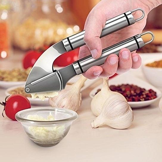 Hand using a garlic press with garlic and ingredients on a kitchen counter